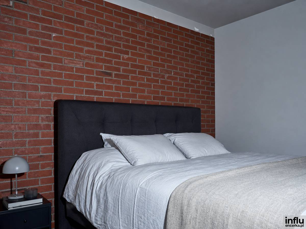 Ściana z czerwonej cegły klinkierowej za łóżkiem w sypialni loft z jasną pościelą