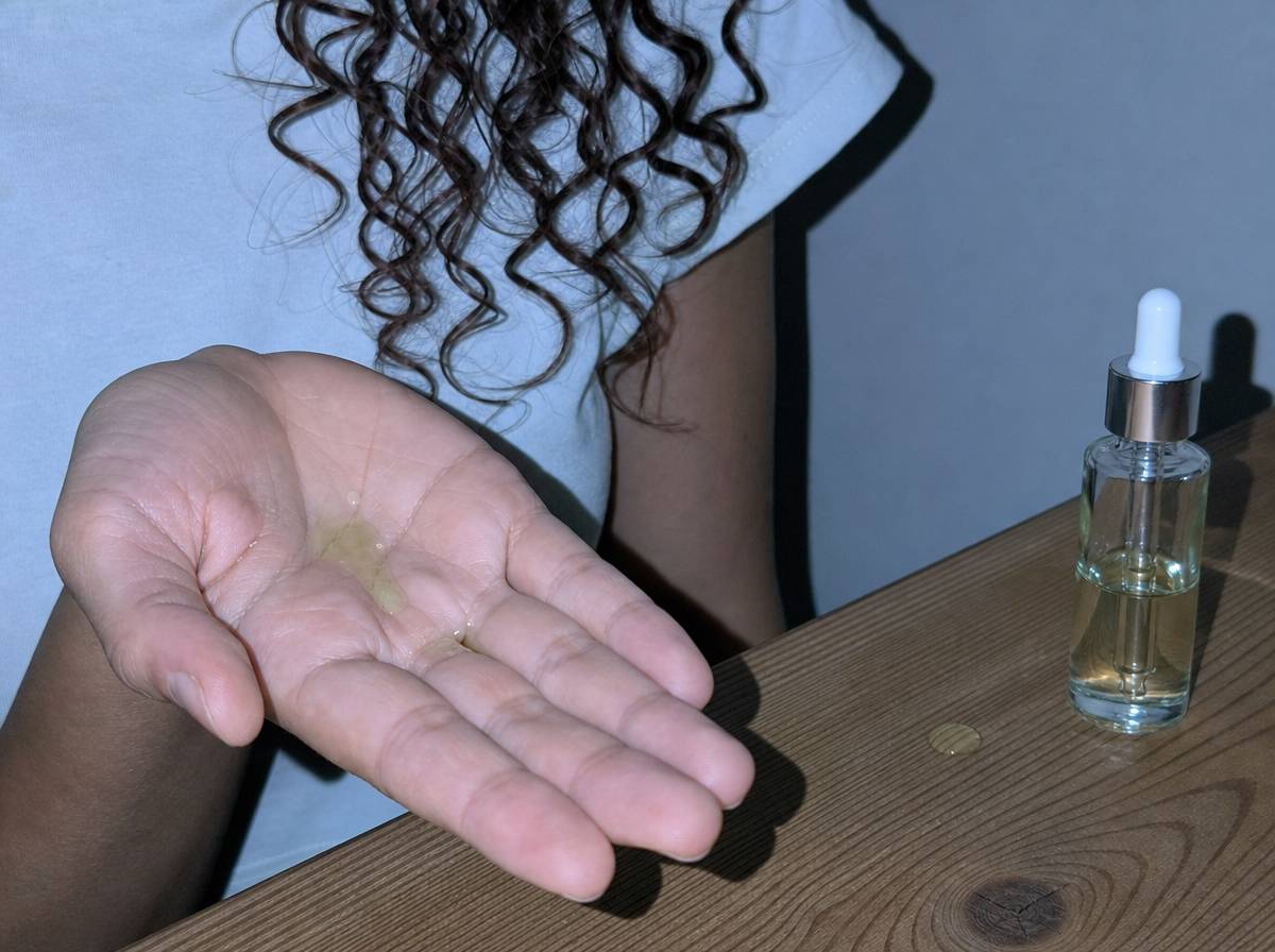 Kilka kropli lekkiego oleju na dłoni obok cienkich, drobno skręconych loków niskoporowatych